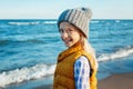 Portrait of smiling blonde white Caucasian child kid girl with long hair, wearing yellow jacket gilet and grey hat Royalty Free Stock Photo