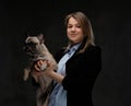 Portrait of a smiling blonde woman breeder holds her cute pug. Isolated on dark textured background.