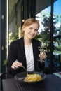 Portrait of a smiling blonde woman eating Italian pasta carbonara and wine at cozy italian restaurant outdoors. Royalty Free Stock Photo