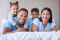 Portrait of a smiling boy and girl lying on their parents in a bed at home. Mixed race couple bonding with their son and Royalty Free Stock Photo