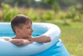 Portrait of smiling boy splashing in an inflatable pool on a sunny summer day in nature. Child staying cool in the summer heat