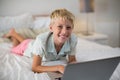 Portrait of smiling boy using laptop on bed in bedroom Royalty Free Stock Photo