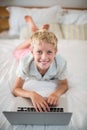 Portrait of smiling boy using laptop on bed in bedroom Royalty Free Stock Photo