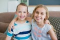 Portrait of smiling brother and sister embracing on couch in living room at home Royalty Free Stock Photo