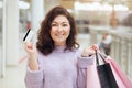 Portrait of smiling brunette female dresses lilac sweater posing in shop with credit card in hand and shopping bags, adorable girl Royalty Free Stock Photo