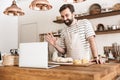 Portrait of smiling brunette man using laptop while cooking in kitchen at home Royalty Free Stock Photo