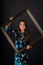 Portrait of smiling brunette woman with bevel on black background. the girl holding frame. She is in black dress with blue flowers Royalty Free Stock Photo