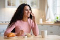 Smiling brunette woman talking on cellphone while having breakfast in kitchen Royalty Free Stock Photo