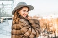 Portrait of smiling brunette woman wearing fur winter coat and grey hat on the background of city Royalty Free Stock Photo