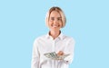 Portrait of smiling business lady holding lots of money over blue studio background, panorama