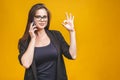 Portrait of smiling business woman phone talking and show OK isolated against yellow background Royalty Free Stock Photo