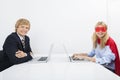 Portrait of smiling businessman with coworker in superhero costume using laptops at office Royalty Free Stock Photo
