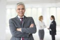 Portrait of smiling businessman standing with arms crossed against colleagues at office Royalty Free Stock Photo