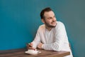 Portrait of a smiling businessman in a white shirt with a phone in his hands, having breakfast in a cafe on a blue background Royalty Free Stock Photo