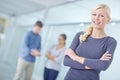 Portrait of a smiling businesswoman standing with her arms crossed and looking at the camera while her colleagues work Royalty Free Stock Photo