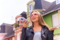 Portrait of a smiling Caucasian blonde woman sending a voice message, against colorful houses