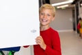 Portrait of smiling caucasian elementary schoolboy holding locker door while standing in school