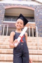 Portrait of smiling caucasian elementary schoolgirl with mortarboard showing degree certificate Royalty Free Stock Photo