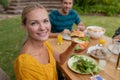 Portrait of smiling caucasian woman holding hamburger eating meal with family in garden