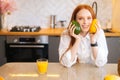 Portrait of smiling charming attractive redhead young woman holding in hands mango and avocado sitting at table in Royalty Free Stock Photo