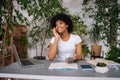 Portrait of smiling charming black female talking on smartphone sitting at desk with laptop computer, paper copybook in Royalty Free Stock Photo