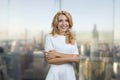 Portrait of smiling cheerful blonde lady with folded arms pointing at copy space with her finger.