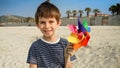 Portrait of smiling cheerful boy with colorful spinning pinwheel on sandy sea beach. Concept of summer holiday, happiness, joy, Royalty Free Stock Photo