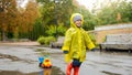 Portrait of smiling cheerful toddler boy running over puddle at park with his toy truck Royalty Free Stock Photo
