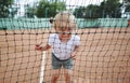 Portrait of the smiling child through a tennis net. Little cute girl in a white T-shirt at tennis court. Royalty Free Stock Photo