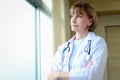 Portrait of smiling confident female doctor in white workwear with stethoscope, standing with arms crossed and looking through the Royalty Free Stock Photo