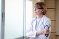 Portrait of smiling confident female doctor in white workwear wearing glasses, holding stethoscope, standing with arms crossed by Royalty Free Stock Photo