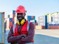 Portrait of a smiling container worker or foreman wearing a red hard hat and folded arms over a blurred container background Royalty Free Stock Photo