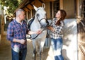 Smiling couple with white horse standing at stable outdoor Royalty Free Stock Photo