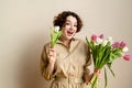 portrait of a smiling curly girl with tulips on a beige background in a beige dress. copy space, pastel color palette