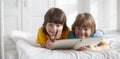 Portrait of a smiling cute brother reading a book lying and relax in bed in a bright white room Royalty Free Stock Photo