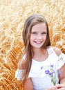 Portrait of smiling cute little girl child on field of wheat holding flowers