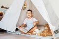 Portrait of smiling cute little preschooler boy reading book to his toys sitting in cozy kids teepee tent in the Royalty Free Stock Photo