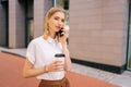 Portrait of smiling cute young blonde woman in fashion clothes holding cup with takeaway coffee to go and talking on Royalty Free Stock Photo