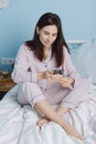 Portrait of smiling cute young mixed race woman blogging, shopping online sit on bed in light modern interior bedrooom