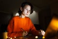 Portrait of smiling designer girl, working at graphic tablet on laptop. Wearing eyeglasses and orange sweater. In dark room home. Royalty Free Stock Photo