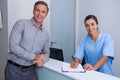 Portrait of smiling doctor holding pen standing by man at desk Royalty Free Stock Photo