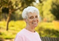 Portrait of smiling elderly woman at park. Happy thoughful mature woman relaxing outdoor.