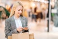 Portrait of smiling elegance blonde young woman in stylish jacket using mobile phone holding shopping paper bags with Royalty Free Stock Photo
