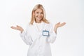 Portrait of smiling, energetic medical employee, female doctor shrugs and laughs, stands in clinic uniform, white