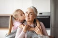 Portrait of smiling european little granddaughter kisses cheek of elderly grandmother in apron Royalty Free Stock Photo