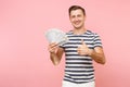 Portrait of smiling excited young man in striped t-shirt holding bundle lots of dollars, cash money, ardor gesture on