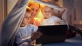 Portrait of smiling family in pajamas hiding in tent at bed and watching video on tablet computer. Family having time together, Royalty Free Stock Photo