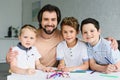 portrait of smiling father and sons at table with papers and colorful pencils