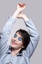 Portrait of smiling female in blue jacket with hands up. Woman with unusual beauty makeup and wet hair, and blue shadows make-up