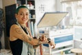 Smiling female worker standing on background of print machine in design studio and looks camera Royalty Free Stock Photo